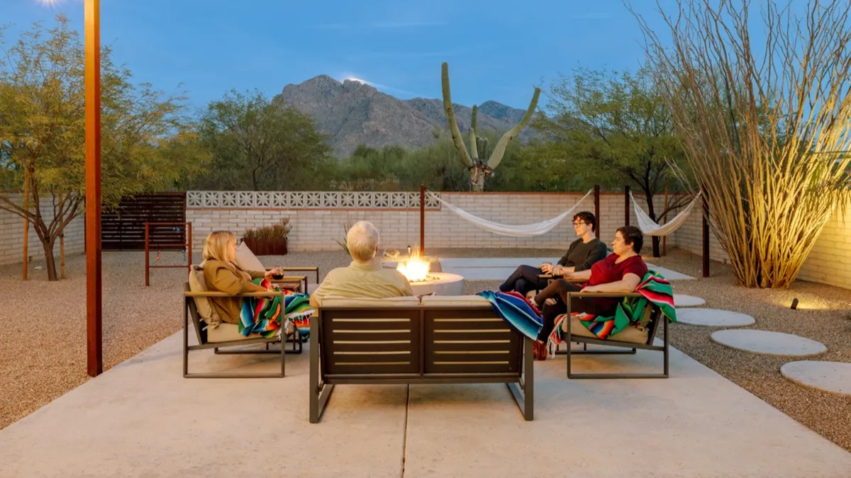 This exterior shot captures a lively group gathered around a fire pit, framed by comfortable seating and hammocks. In the background, the mountain view amplifies the sense of desert tranquility and connection with nature. The communal atmosphere is enhanced by the relaxed postures of people enjoying both the fire and the hammocks.
