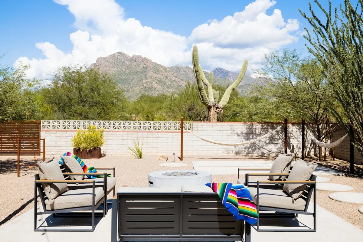 A tranquil patio with a glowing fire pit, comfortable seating, and a breathtaking desert mountain view. The golden hour light casts a romantic glow, highlighting native cactus plants and the expansive sky—ideal for sunset watching or sharing a meal outdoors.