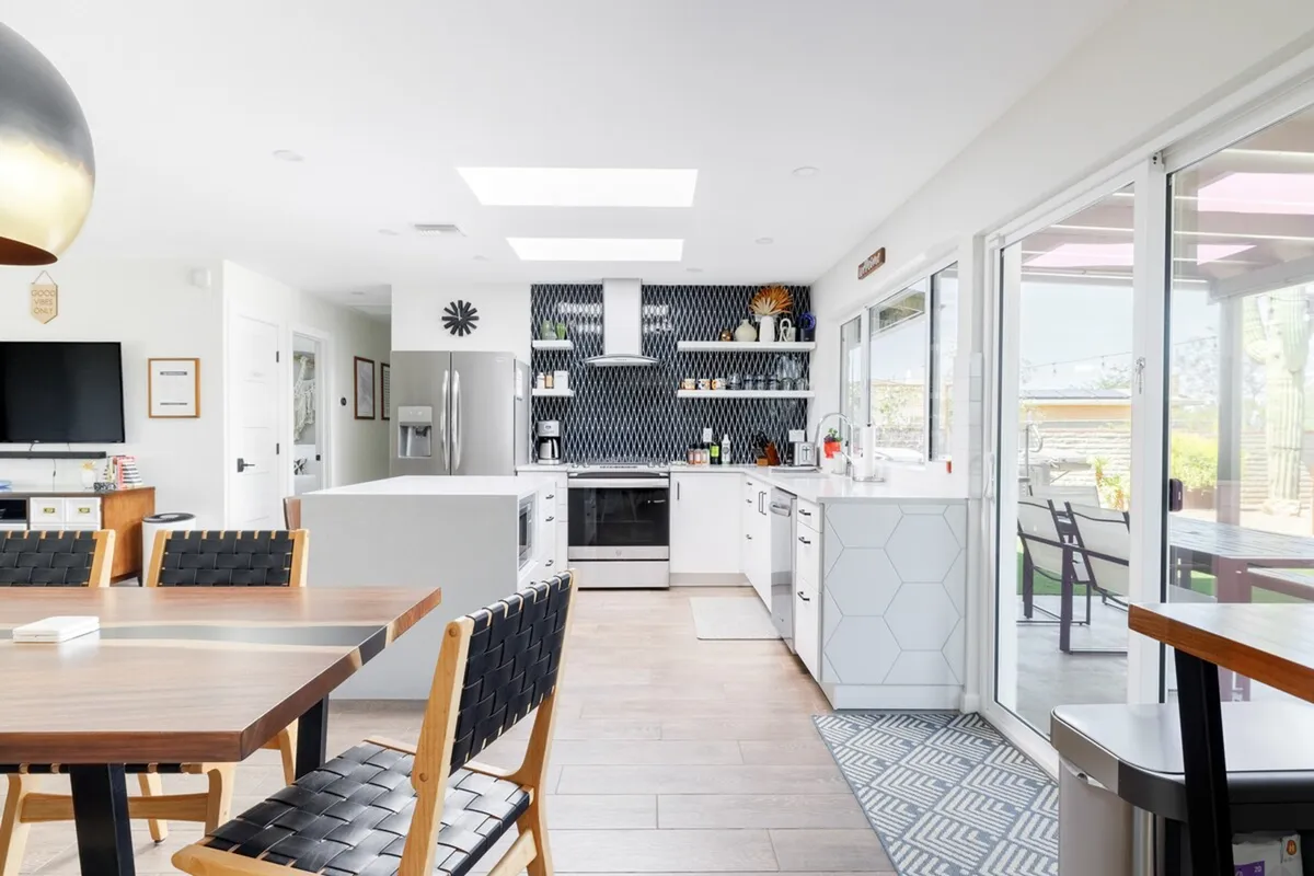 A bright, welcoming kitchen and dining area featuring a kitchen island, geometric backsplash, and a dining table set up for shared meals. The space is designed for communal cooking, dining, and entertaining.