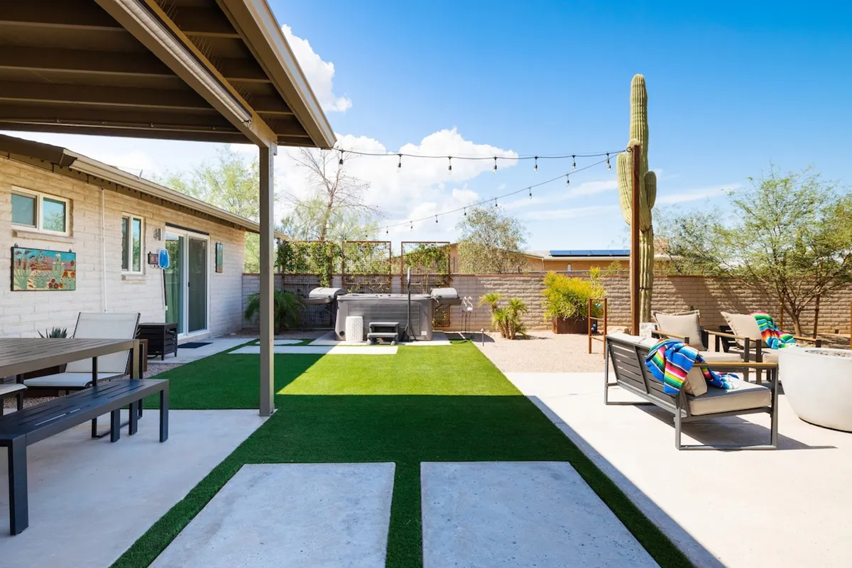 A stylish exterior seating area with a hot tub, string lights, cacti, and wall art, all arranged for casual relaxation and hosting guests. The space is perfect for stargazing or celebrating special moments outdoors.