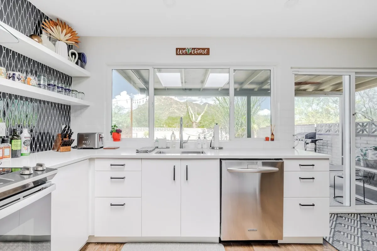 A contemporary kitchen with sleek cabinetry and expansive windows offers a breathtaking view of the desert landscape. Decorative wall art and ample natural light enhance the inviting atmosphere, making this an ideal spot for morning coffee or entertaining guests.