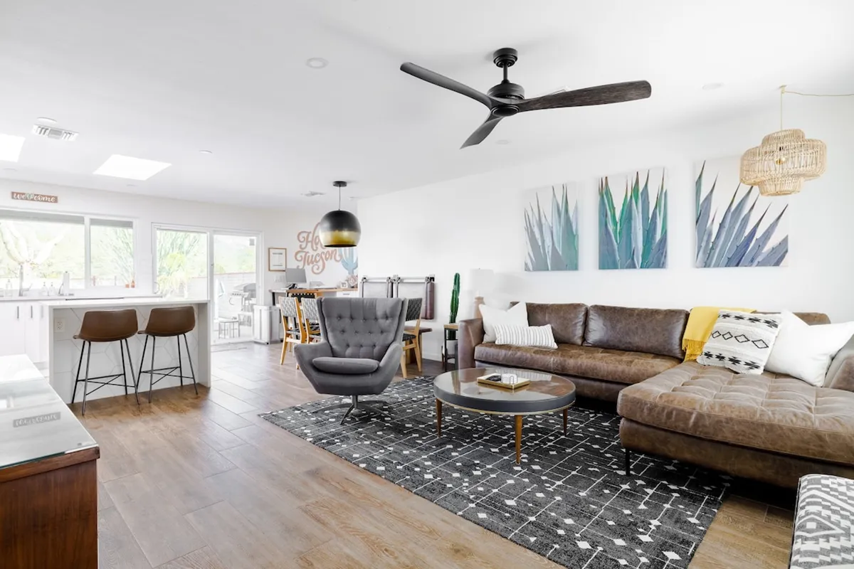 A contemporary living room with a modern sectional sofa, a stylish armchair, a round coffee table, and colorful artwork on the wall. The area feels cozy and sociable, designed for casual gatherings and storytelling.