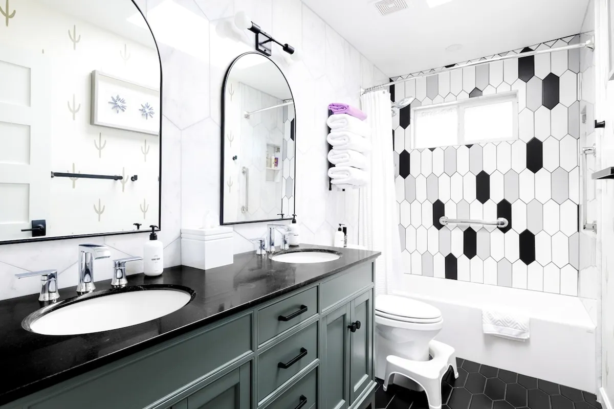 A modern bathroom featuring double sinks, large mirrors, a distinctive hexagonal tile accent wall, and a bathtub. The space is bright, clean, and inviting, suggesting a spa-like atmosphere that invites self-care and relaxation.